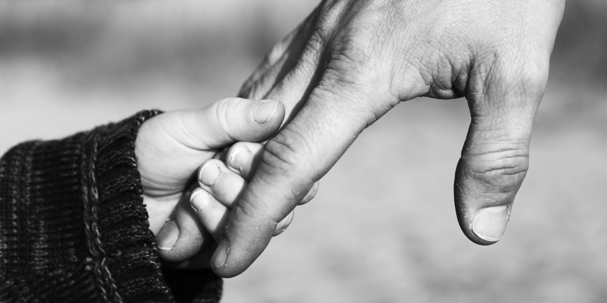 A close up image of a child's small hand holding his father's hand. Black and white mage with some graininess.
